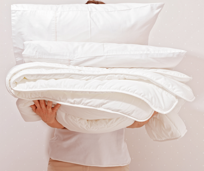 Image of person holding a pile of bedding and pillows